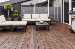 Bright garden furniture, grill and plants on cozy terrace with wooden floor and brick wall